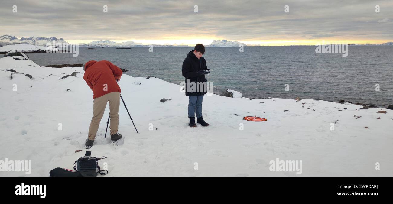 Due persone stanno preparando attrezzature per la fotografia e un drone che vola in un fiordo vicino a Lodingen sulle isole Lofoten, Norvegia. Paesaggio invernale. Foto Stock