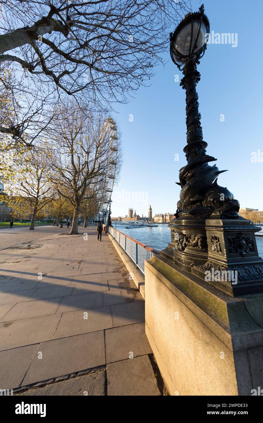 Regno Unito, Londra, lampada ornata lungo la Queen's Walk con il London Eye e il Palazzo di Westminster in lontananza. Foto Stock