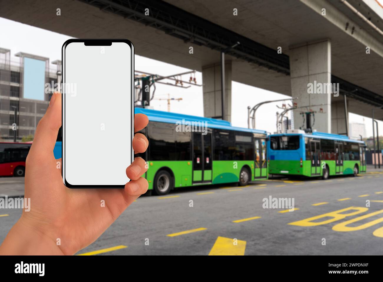 Una mano con un telefono sullo sfondo di un bus elettrico di ricarica. Foto Stock