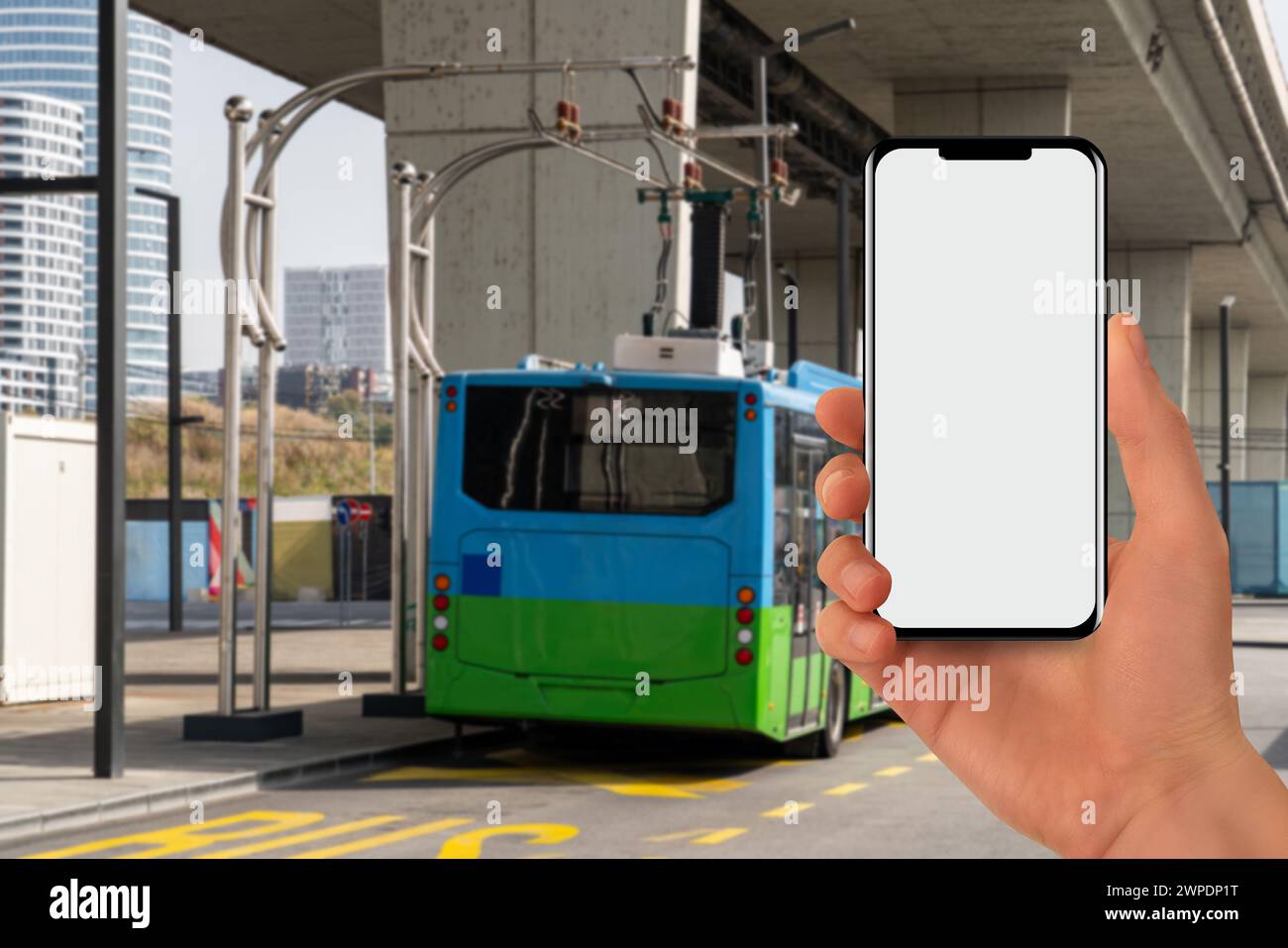 Una mano con un telefono sullo sfondo di un bus elettrico di ricarica. Foto Stock