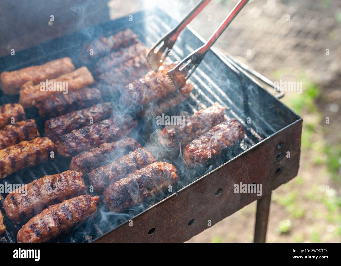 Piccoli involtini rumeni sminuzzati chiamati mici o mititei, simili ai cevapi serbi, salsicce fresche balcaniche senza pelle, cotte all'aperto sul barbecue Foto Stock