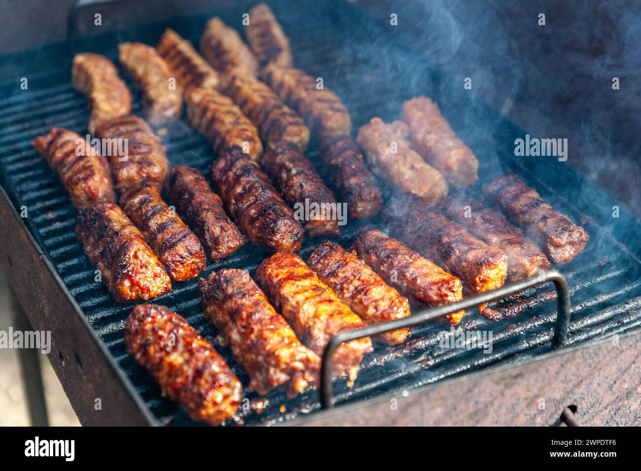 Piccoli involtini rumeni sminuzzati chiamati mici o mititei, simili ai cevapi serbi, salsicce fresche balcaniche senza pelle, cotte all'aperto sul barbecue Foto Stock