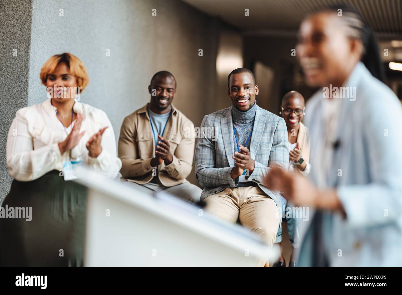 Un gruppo di professionisti è seduto e applaude entusiasticamente in un moderno ambiente di ufficio. Stanno partecipando a un seminario, mostrando supporto e. Foto Stock