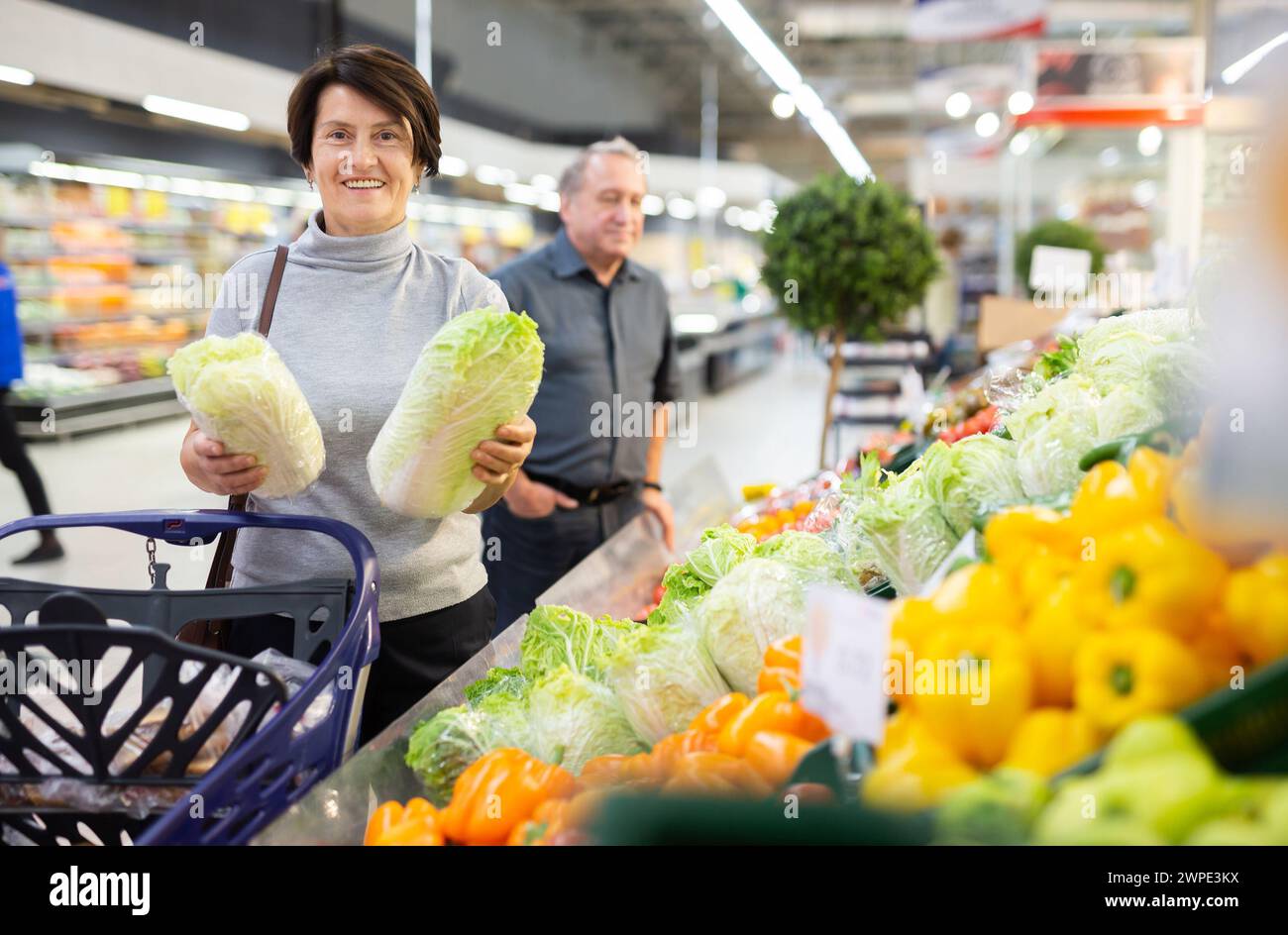 La donna anziana esamina il cavolo cinese nella sezione vegetale per scegliere il cavolo più succoso Foto Stock