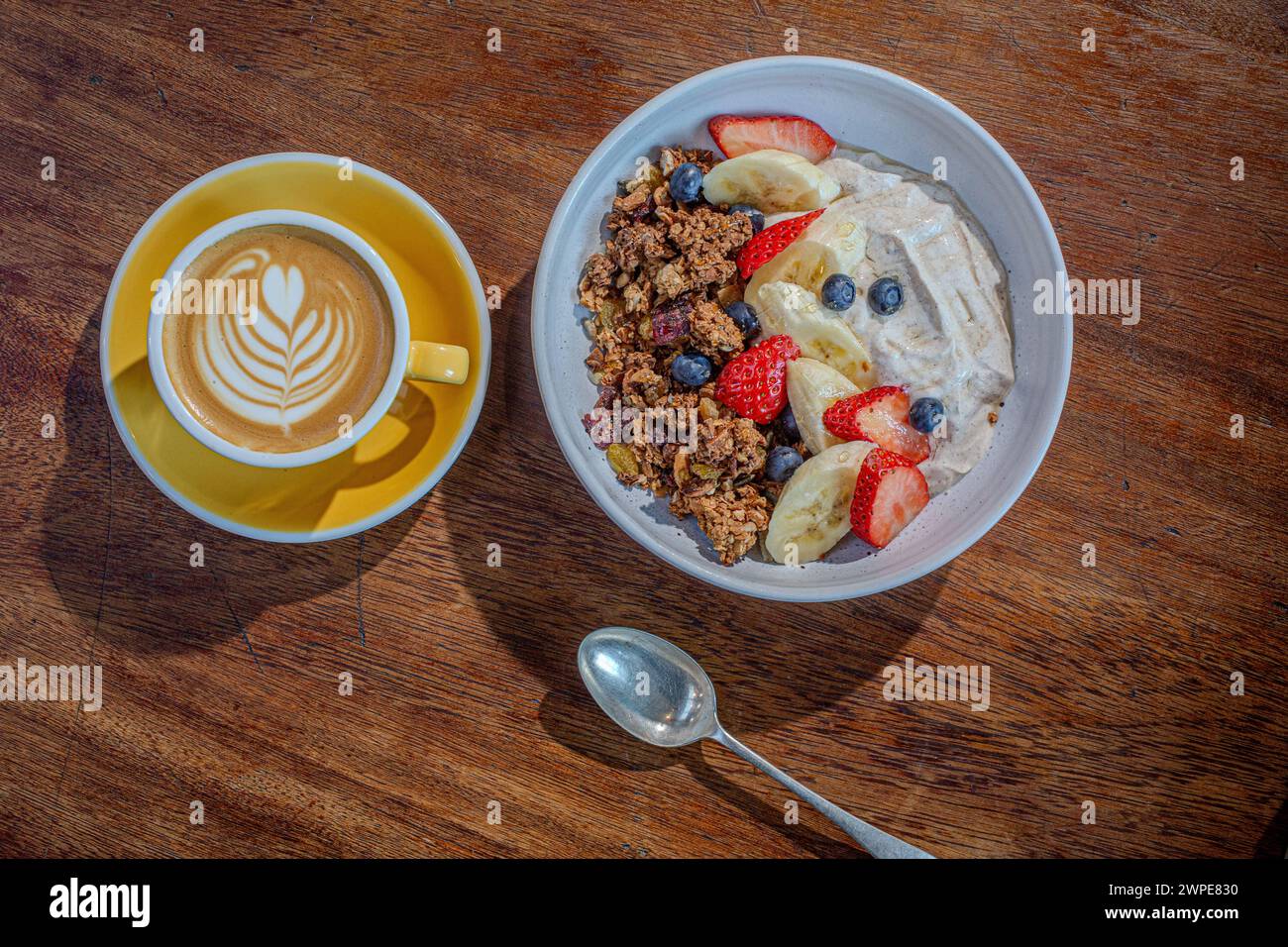 Una tazza di caffè bianco piatto con ciotola di muesli e yogurt su un tavolo di legno nella caffetteria. Foto Stock