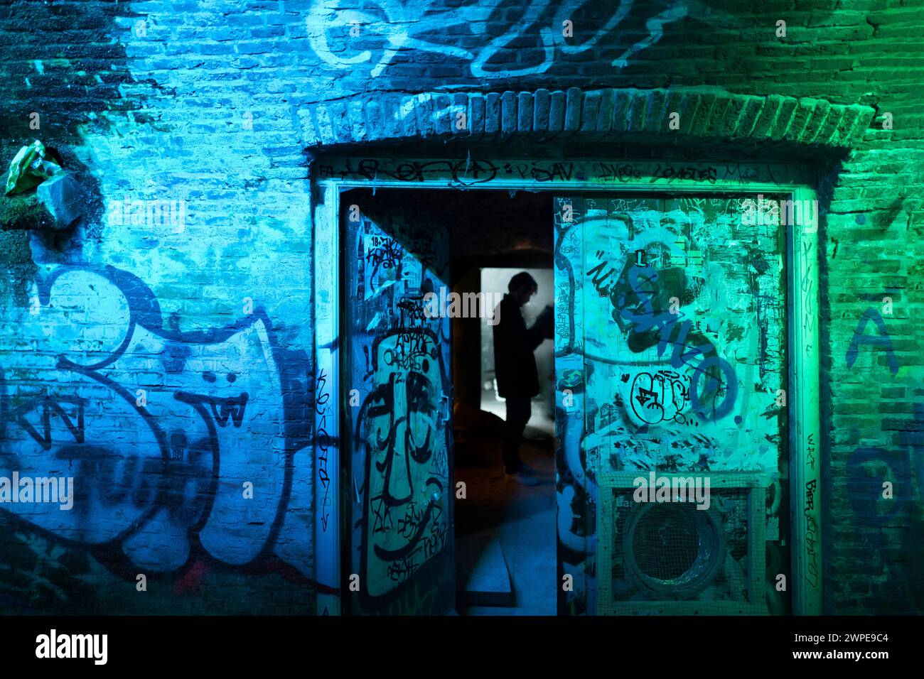 Amsterdam- Paesi Bassi- circa 2019. Posto alla moda e silhouette da uomo in primo piano. Antiche pareti dipinte di graffiti illuminate di colore blu. Foto Stock