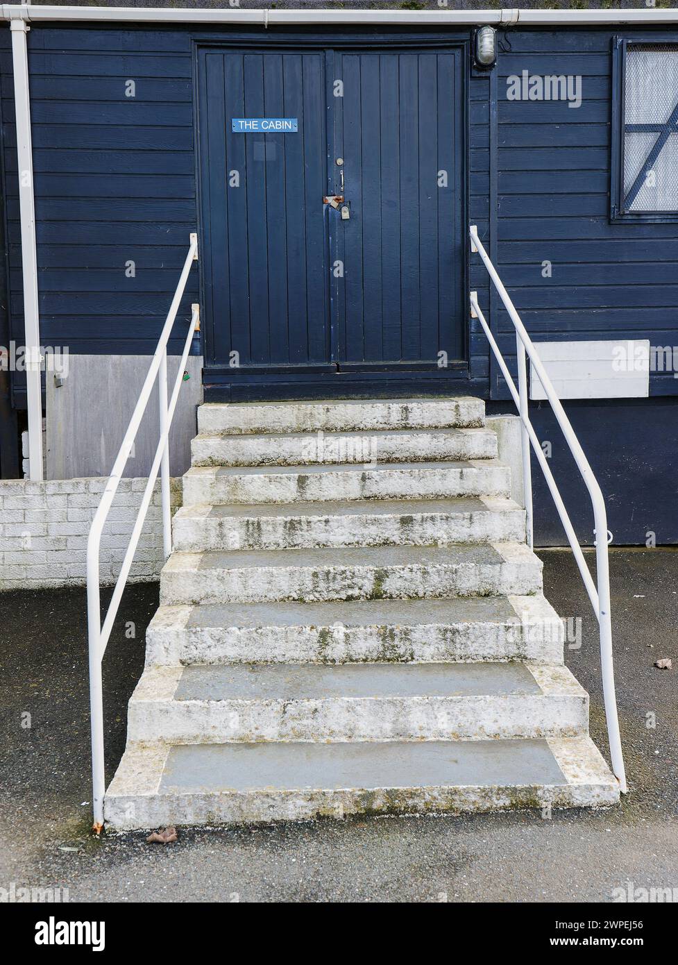 Gradini bianchi con corrimano che conducono alla cabina in legno dipinta di blu con doppia porta chiusa e cartello sulla porta che dice la cabina e la finestra sul lato della. Foto Stock
