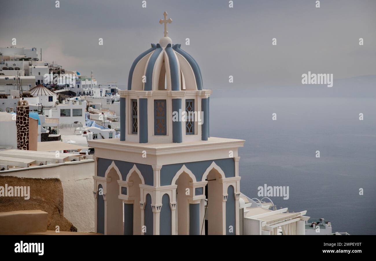 La distinta cupola blu di una chiesa di Santorini si distingue sullo sfondo drammatico di una tempesta imminente. Foto Stock