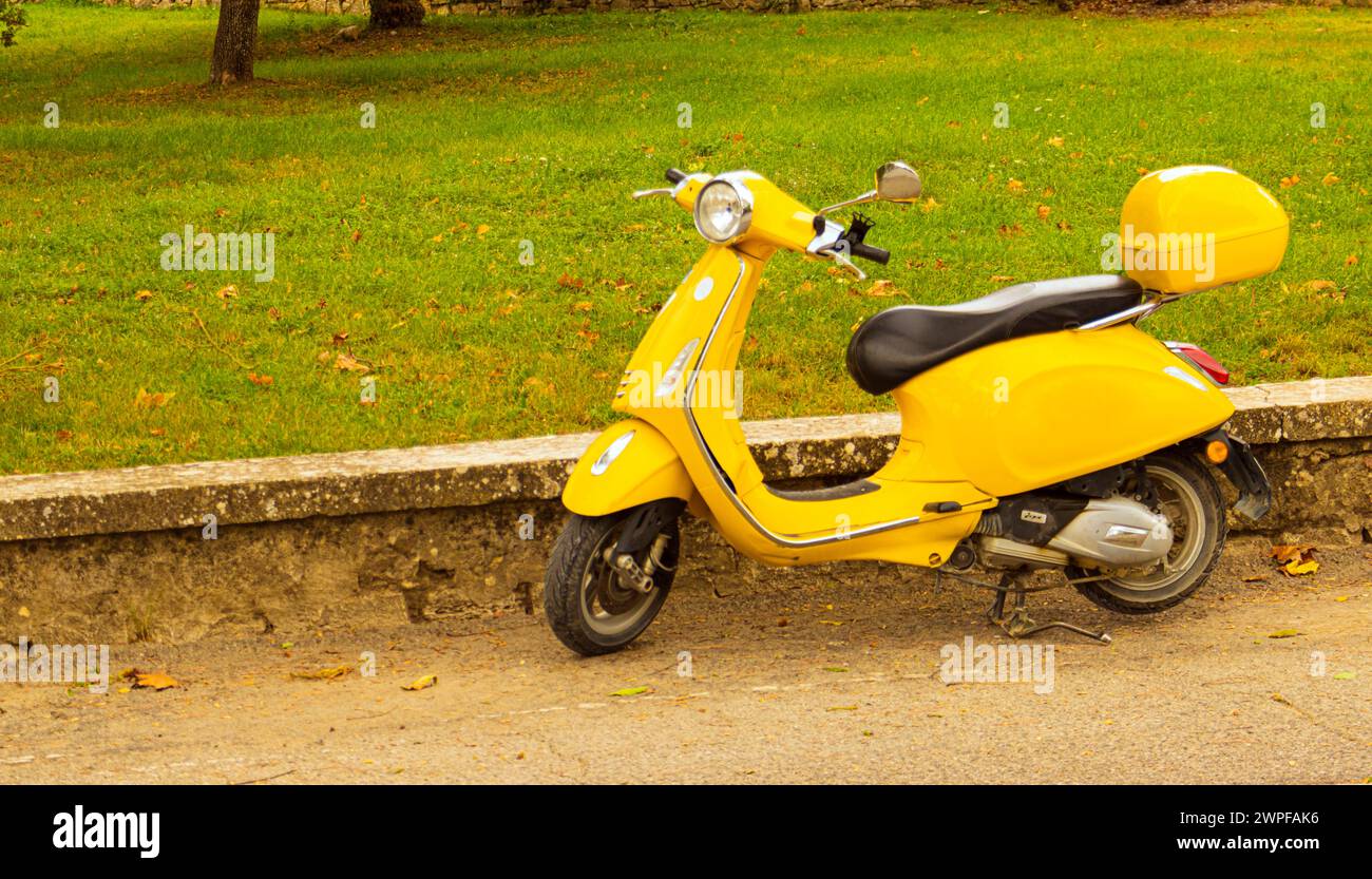 scooter giallo d'epoca parcheggiato sulla strada accanto a un parco. Foto Stock