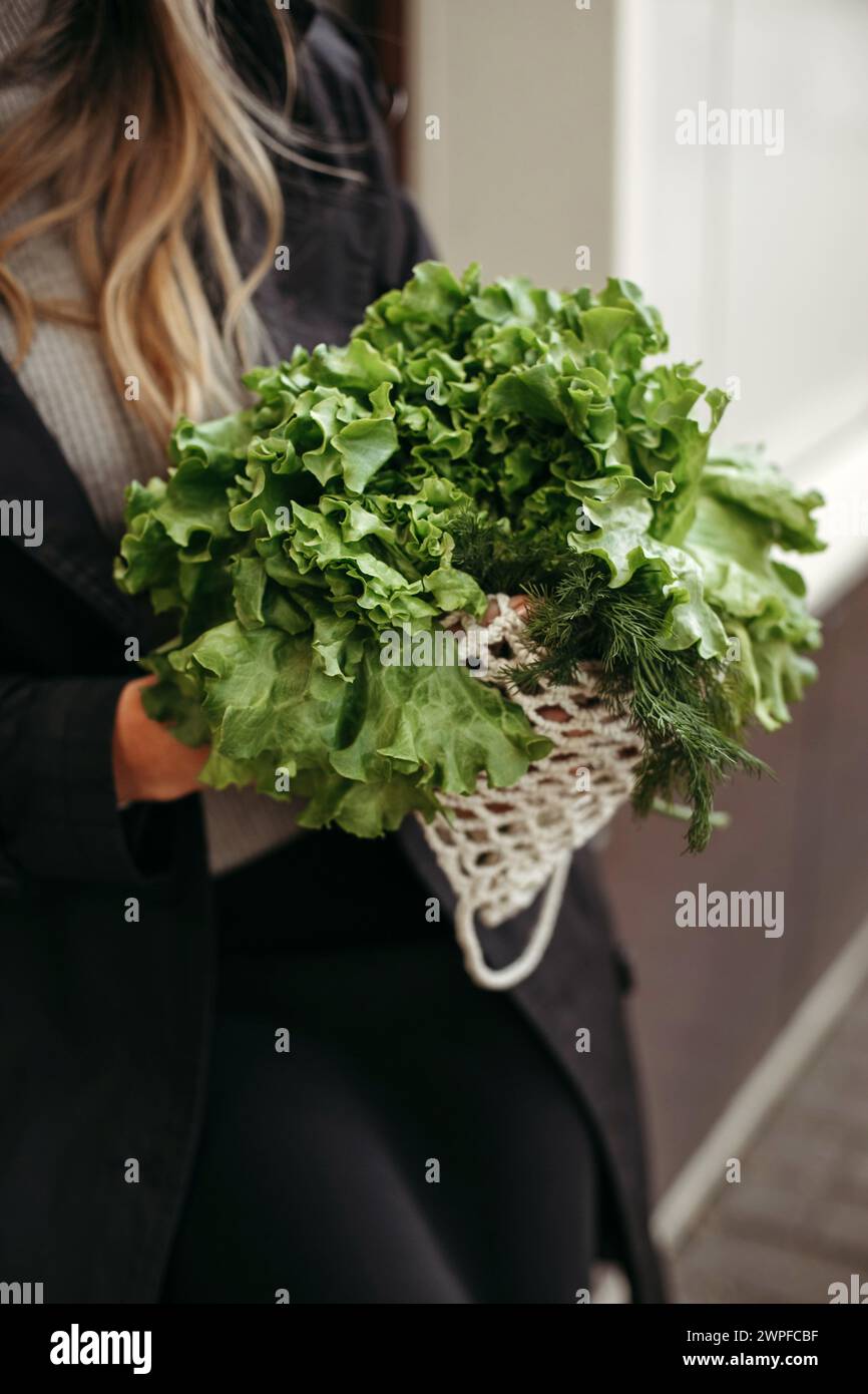 Una donna in piedi mentre tiene in mano un mucchio di verdure verdi fresche. Immagine verticale. Foto Stock