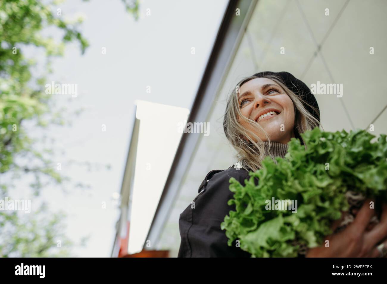 Una donna in piedi all'aperto, che tiene in mano un mucchio di verdure verdi fresche. Foto Stock