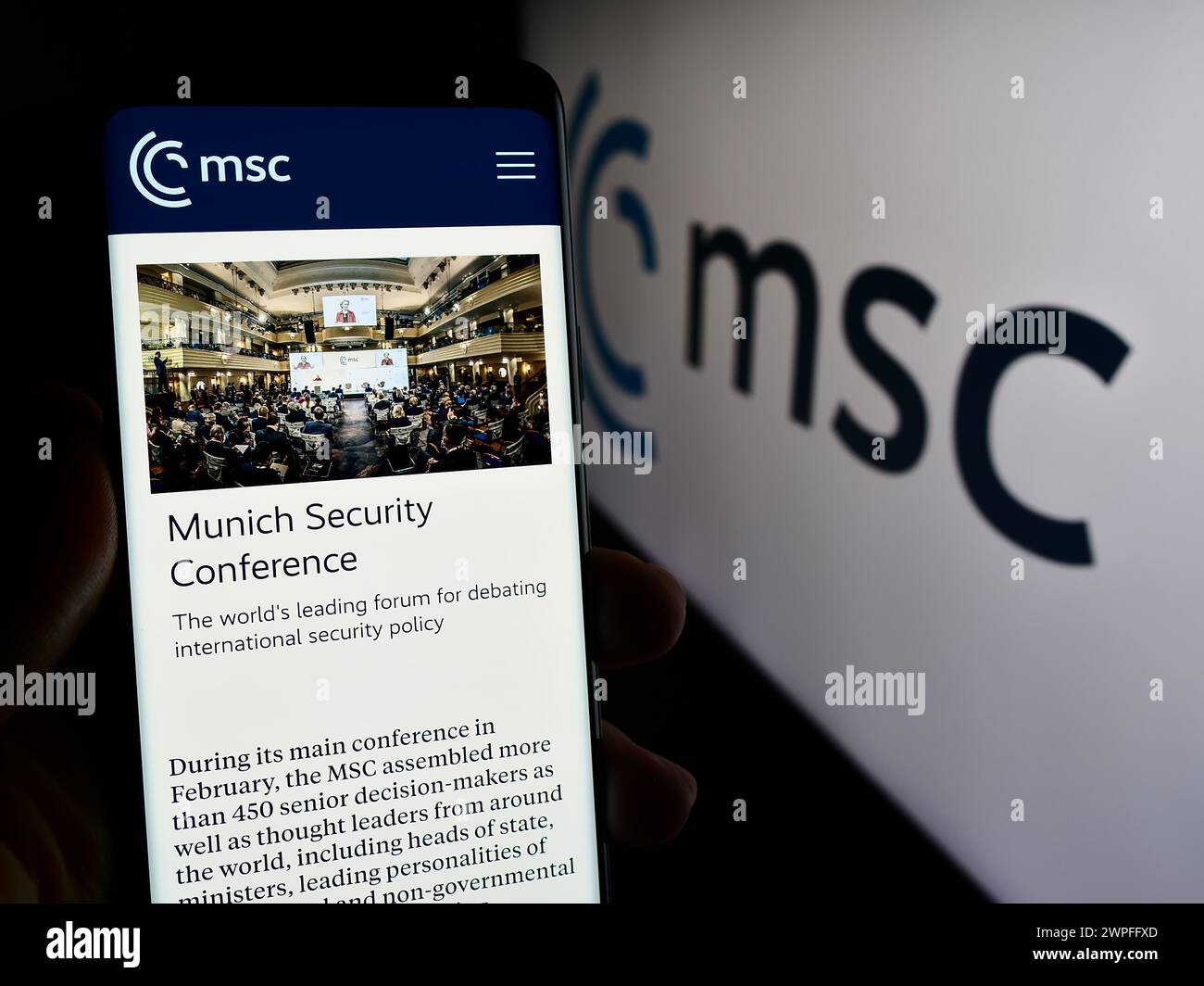 Persona con smartphone con pagina Web dell'evento annuale Munich Security Conference (MSC) davanti al logo. Messa a fuoco al centro del display del telefono. Foto Stock