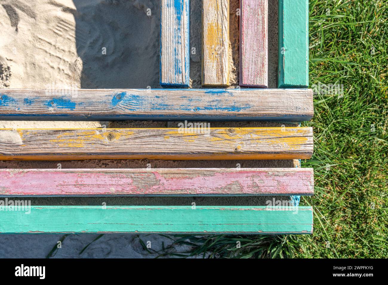 Barriera in cemento con barre di legno colorate che fungono da sedili, che circonda una pozza di sabbia per bambini vicino a un prato lussureggiante nella vista superiore della giornata soleggiata Foto Stock