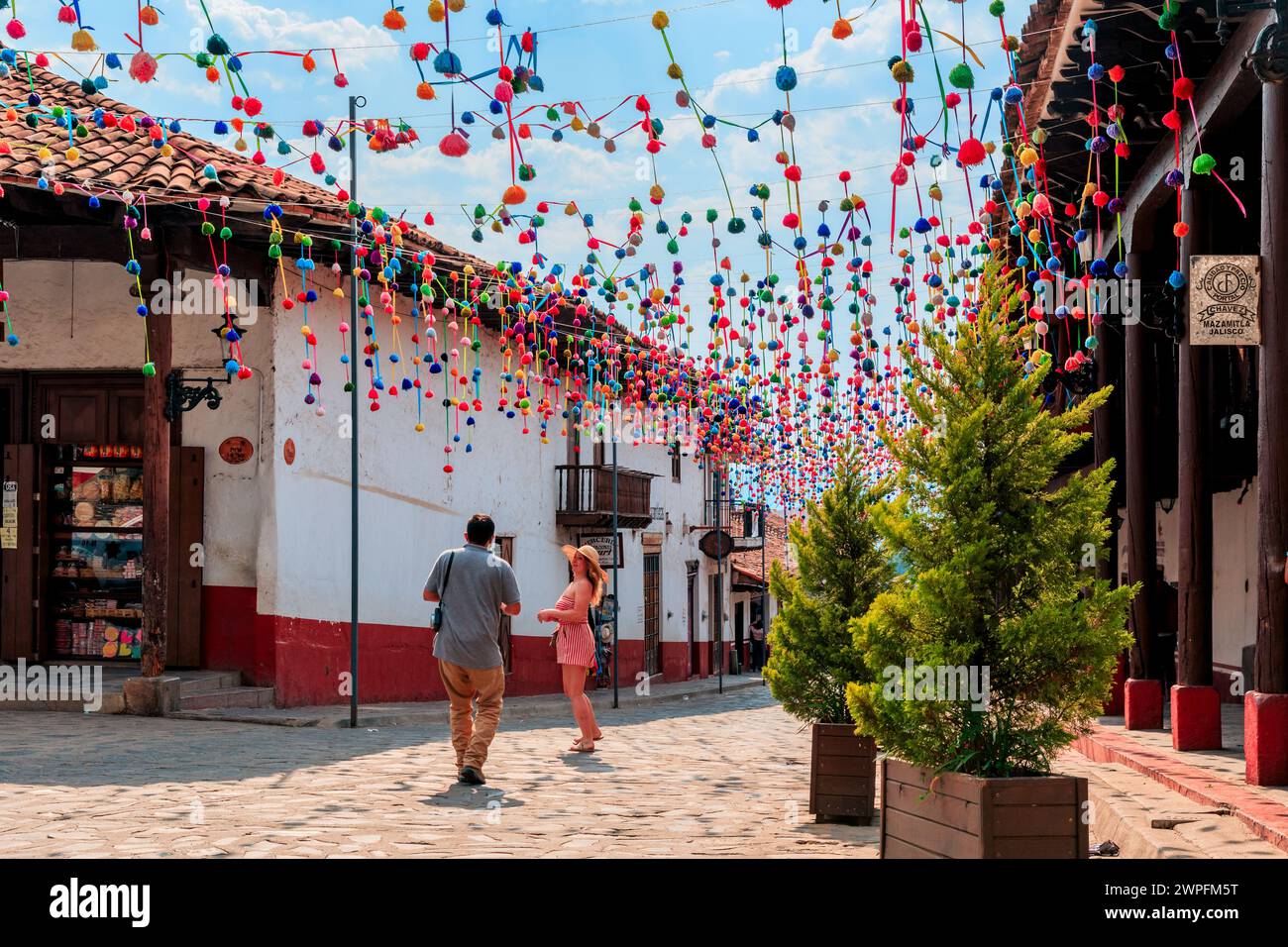 Un gruppo di individui che passeggiano in un colorato spazio all'aperto adornato da vibranti pomponi di carta Foto Stock