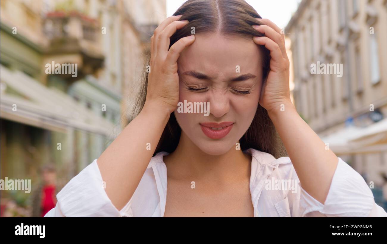 Primo piano giovane donna caucasica europea con mal di testa mal di testa dolore emicranico città fuori infelice stanchezza femminile disagio sofferenza cattiva Foto Stock
