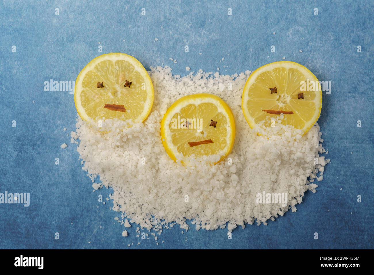 fette di limone con chiodi di garofano e cannella che formano una faccia sorridente su una pila di sale e sfondo blu con spazio di copia Foto Stock