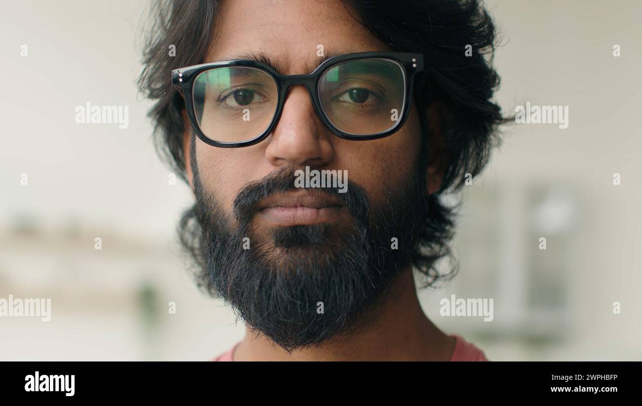 Primo piano uomo arabo musulmano barbuto scapolo proprietario di casa indiano multietnico ragazzo serio guardando la telecamera occhi cattivi visione in occhiali da vista maschio Foto Stock