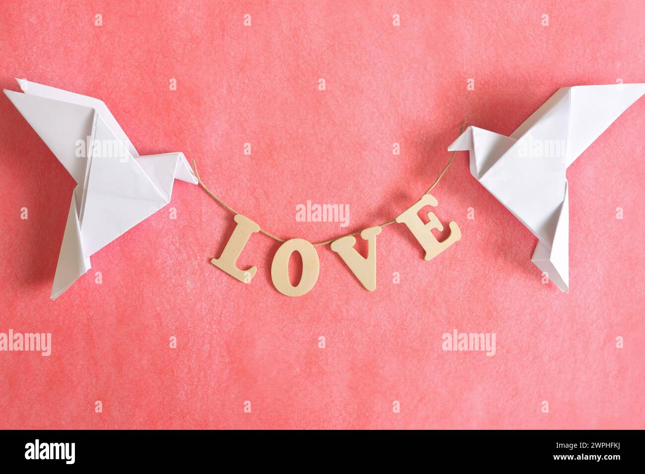 Diffondere il concetto di messaggio d'amore. Due colombe origami bianche che portano la parola AMORE su sfondo rosso. Foto Stock