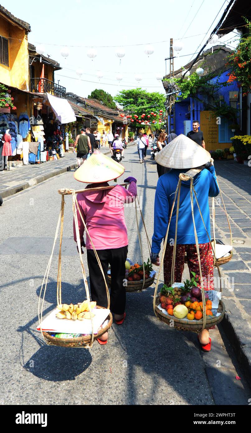 Donne vietnamite che camminano con palo portante con cesti di frutta, chiamato anche palo a spalla, a Hoi An, Vietnam. Foto Stock