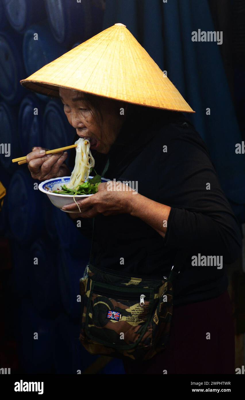 Una donna vietnamita che mangia una ciotola di spaghetti per colazione al mercato del pesce fresco e del pesce di mattina presto a Thanh Hà, Hoi An, Vietnam. Foto Stock