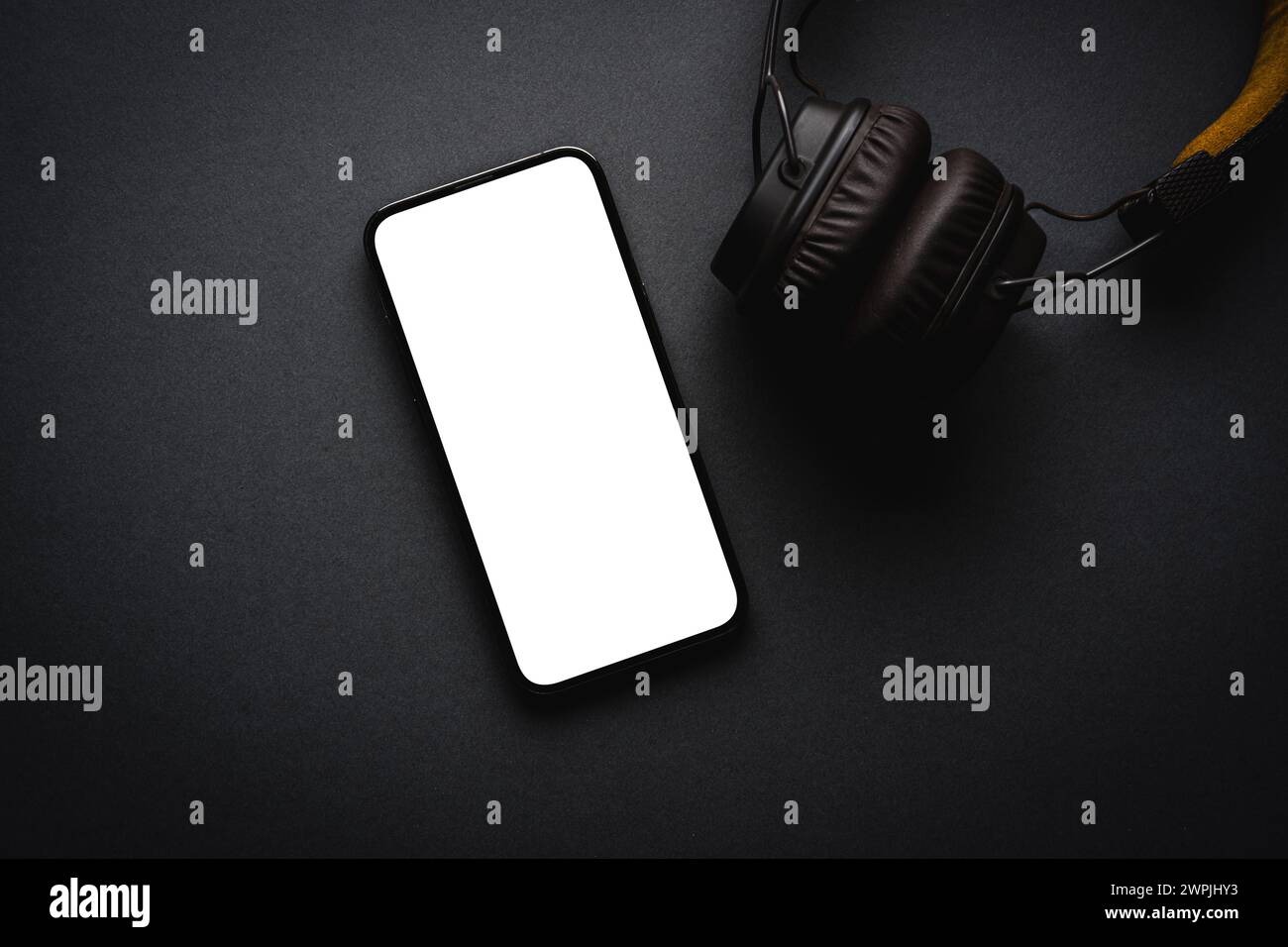 Cuffie wireless avvolgenti in stile retrò e smartphone con schermo vuoto su sfondo grigio scuro Foto Stock