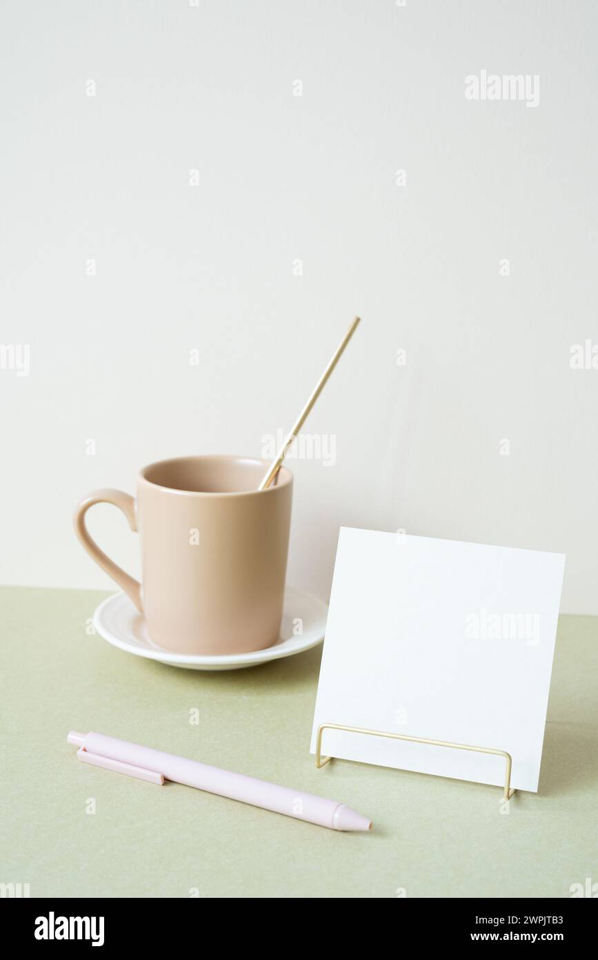 Blocco note vuoto con supporto, penna e tazza sulla scrivania. sfondo bianco avorio. cancelleria per ufficio Foto Stock