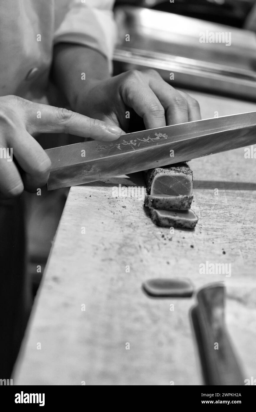 Primo piano dello chef sushi che affetta tonno scottato con un coltello sul tagliere. Foto Stock