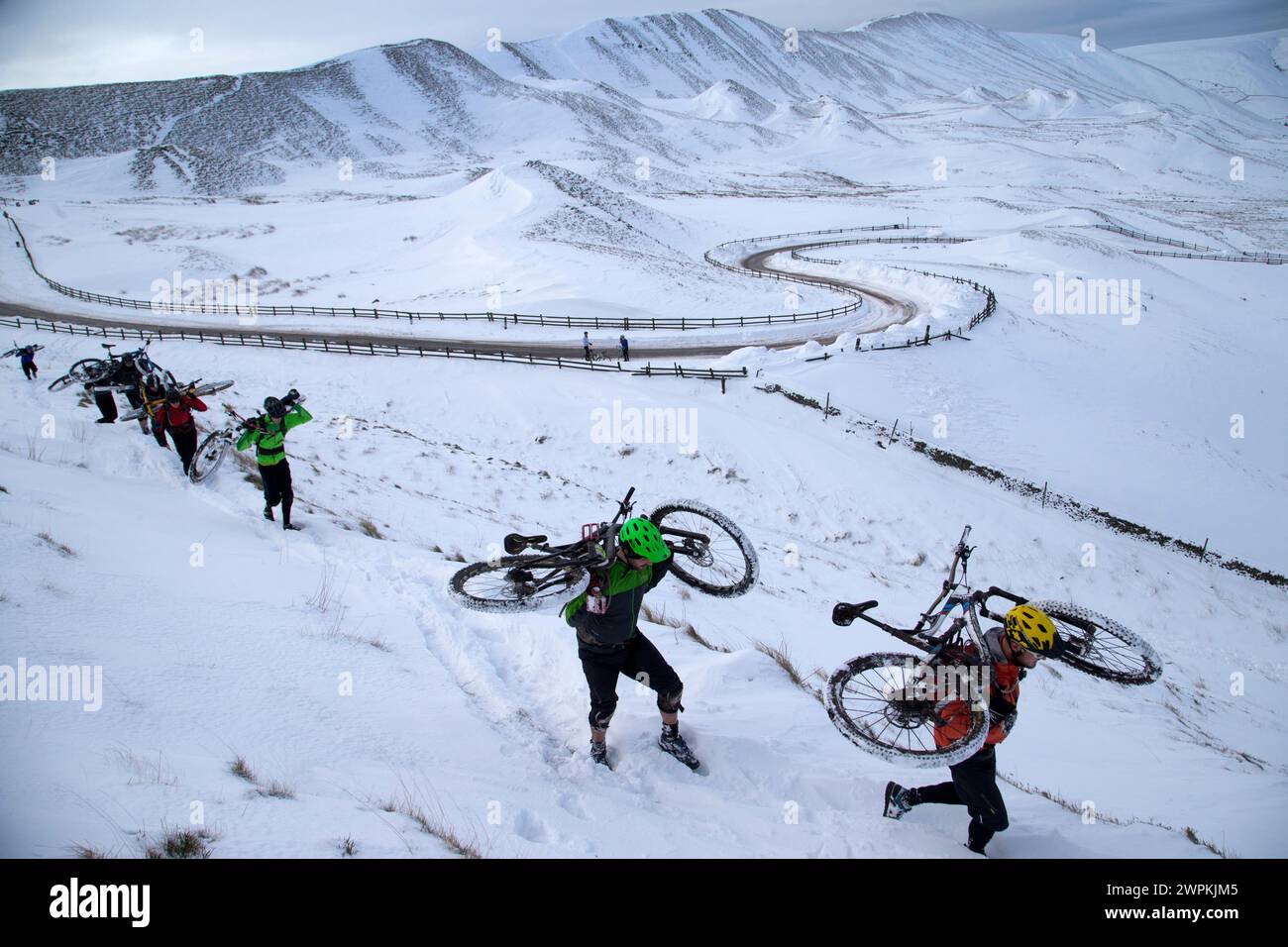 01/02/15 dopo un'altra notte di neve, un gruppo di ciclisti trasporta le loro mountain bike ai margini di Mam Tor, affacciato sulla valle di Edale nel Derb Foto Stock