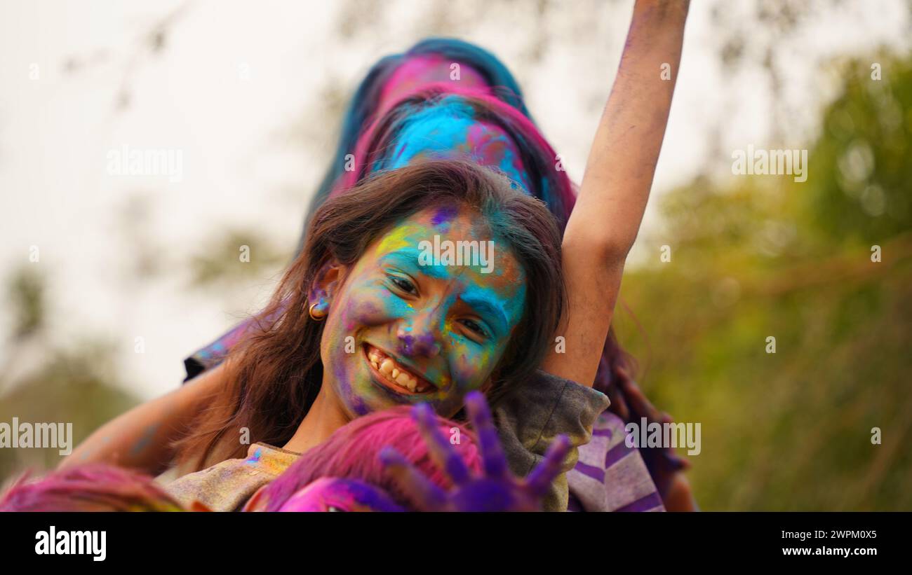 Giovane ragazza allegra e simpatica con polvere di colori holi applicata che mostra mani colorate alla macchina fotografica durante la celebrazione del festival holi Foto Stock