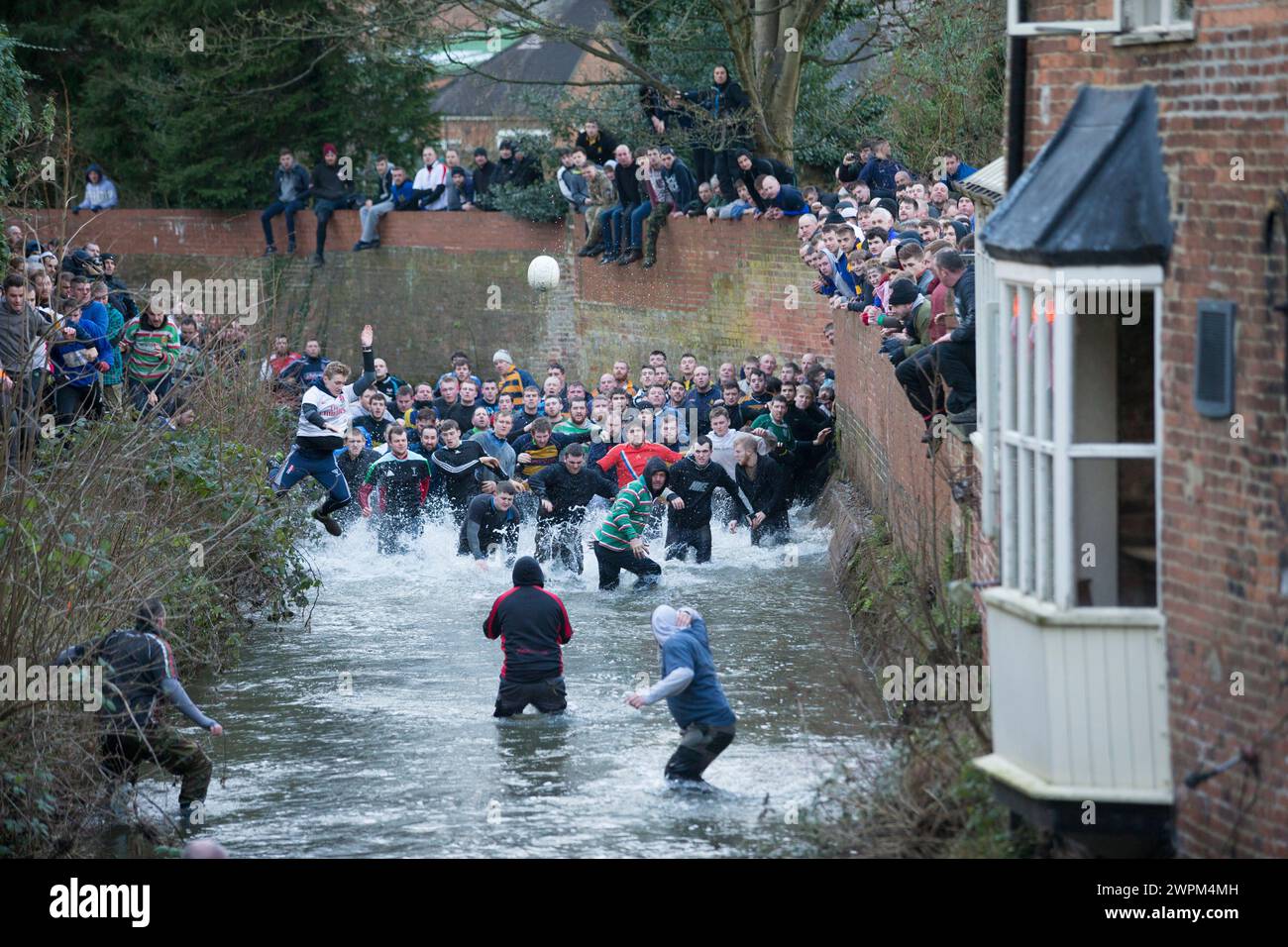 08/02/16 i giocatori inseguono il pallone attraverso Henmore Brook mentre la partita di calcio del Royal Shrovetide viene giocata attraverso la città di Ashbourne, Derbyshire. U' Foto Stock