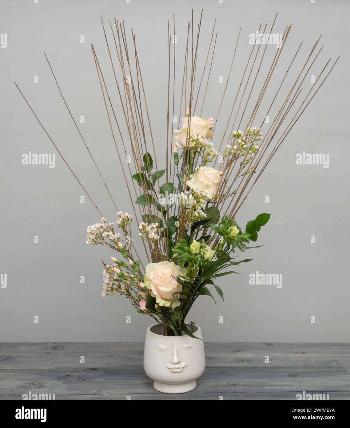 Bouquet legato a mano con rose rosa, fiori di cera, dianthus e anemoni su un telaio a bastoncino di canne, in una fioriera bianca. Foto Stock