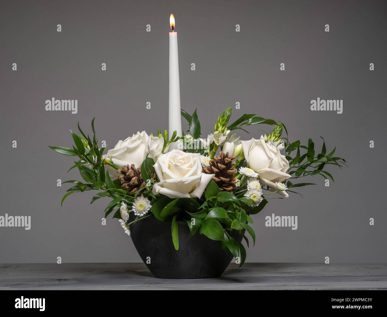 Disposizione dei tavoli floreali con rose bianche e mini crisantemi, fogliame e coni di abete, visti su sfondo grigio. Foto Stock