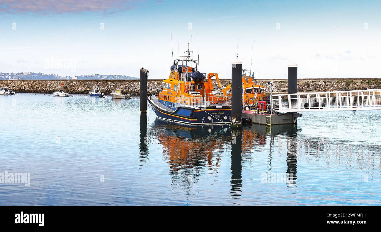 Torbay Lifeboat ormeggiata a Brixham Marina Devon vicino al frangiflutti e alla passerella di accesso alla scialuppa di salvataggio e ai riflessi sull'acqua con un lontano skyline Foto Stock