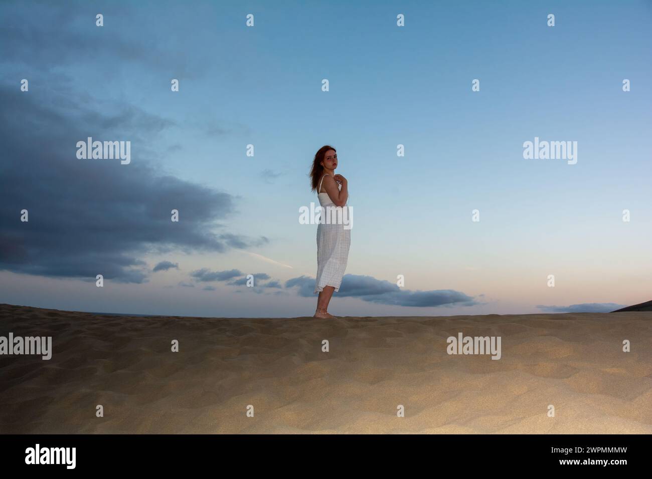 Una giovane donna sta con la schiena tra le dune di sabbia Foto Stock
