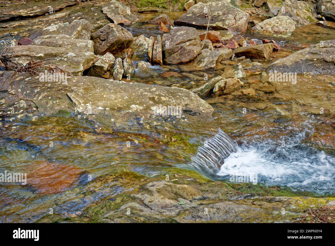 Una vista ravvicinata dell'acqua cristallina che scorre a valle sopra e intorno alle rocce colorate del torrente Foto Stock