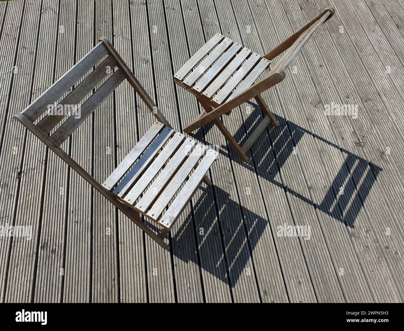 Due sedie di legno si aprono di fronte alla luce del sole su una terrazza di legno Foto Stock