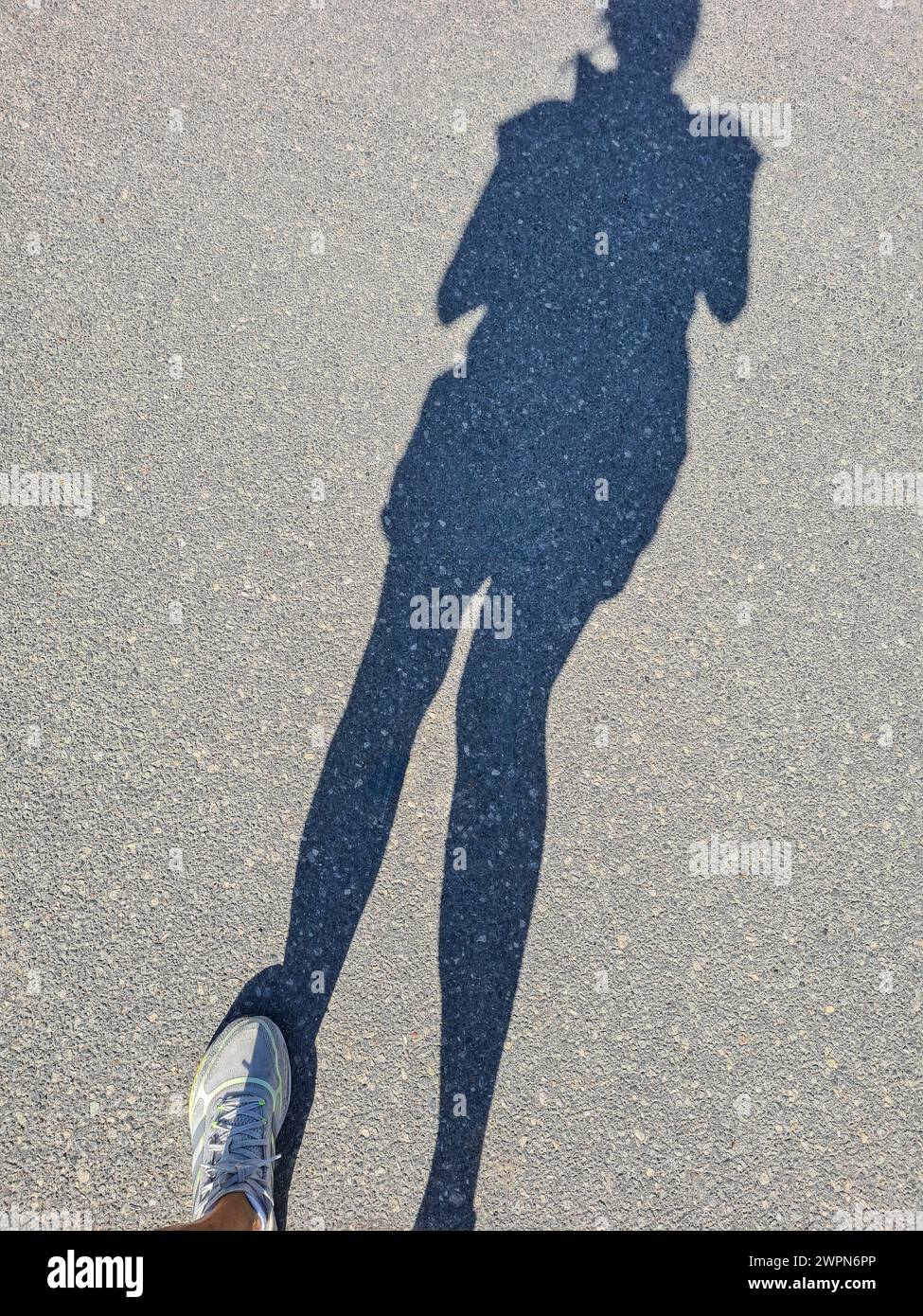 Solo l'ombra di una donna e la sua scarpa sportiva bianca sinistra possono essere viste sulla superficie della strada Foto Stock