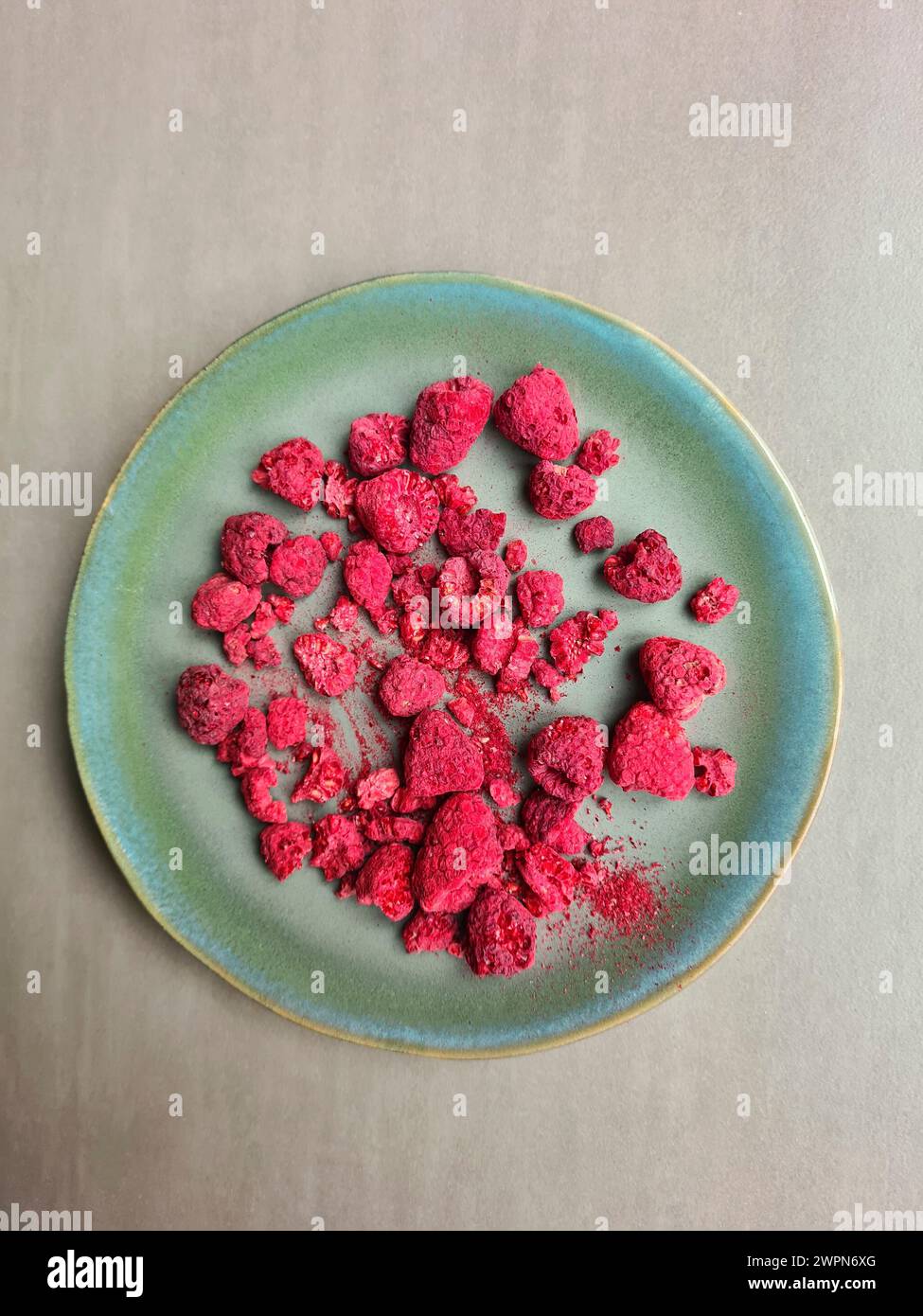 Un piatto verde con lamponi rossi secchi su sfondo grigio Foto Stock