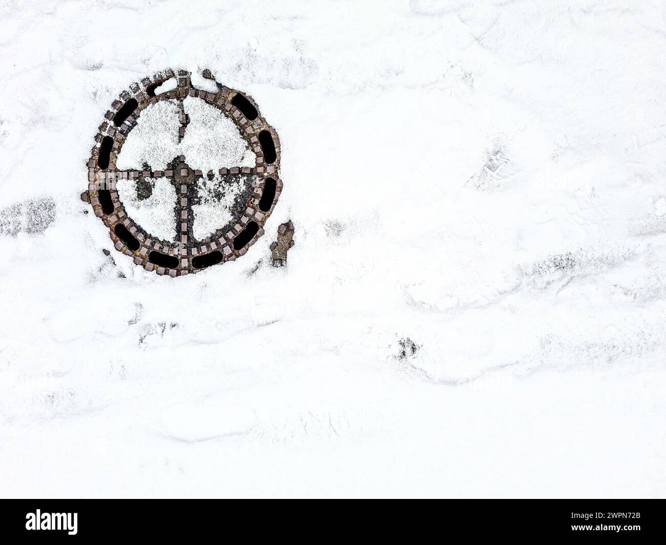 Il tombino ricoperto di neve, così come le piste e i motivi sulla neve creano un'immagine grafica astratta invernale Foto Stock