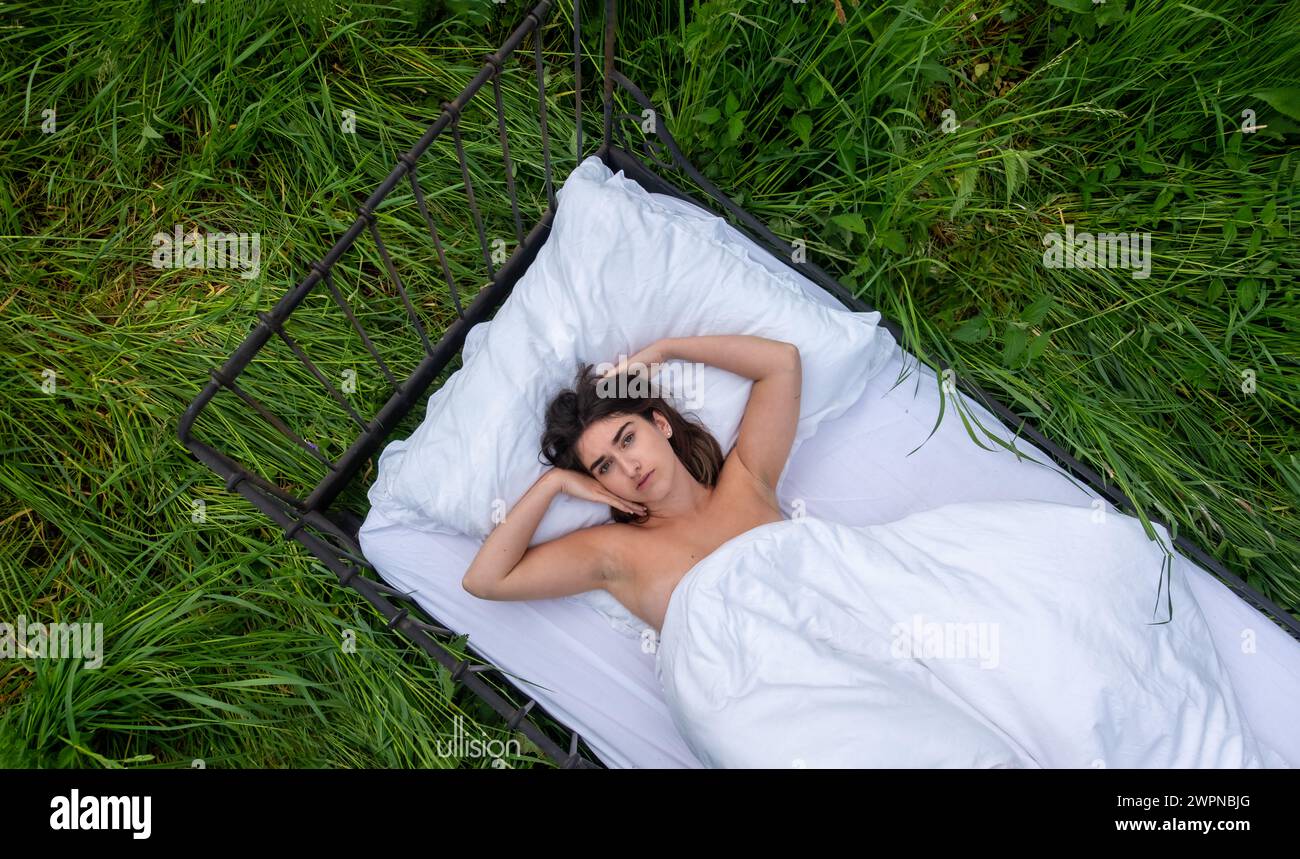 giovane e sexy nuda bruna a letto su un prato verde e soleggiato estivo, copia spazio Foto Stock