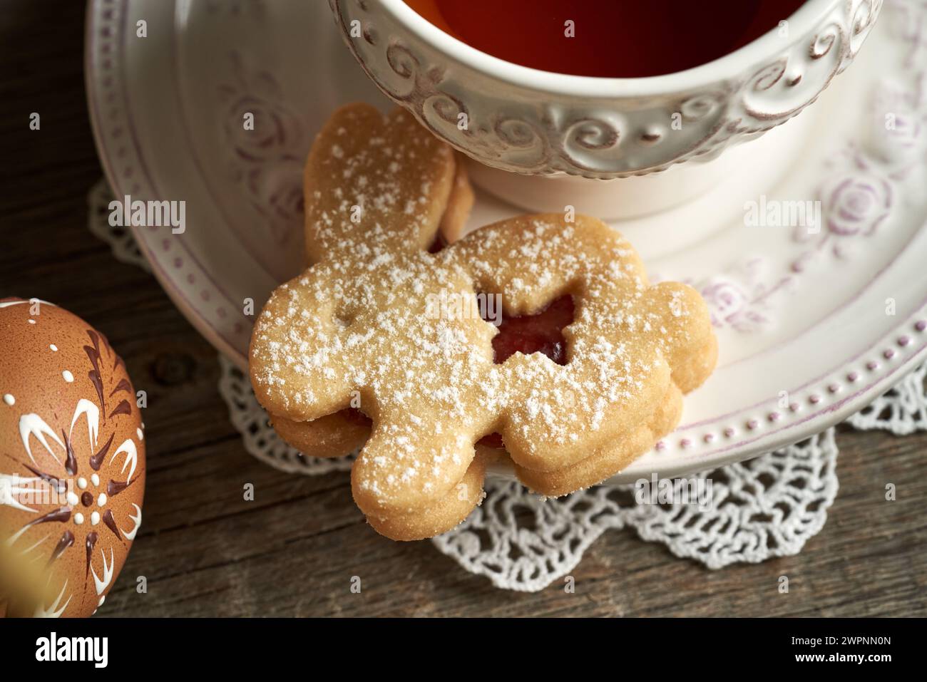 Biscotto pasquale Linzer a forma di coniglietto con una tazza di tè e uovo decorato con cera Foto Stock