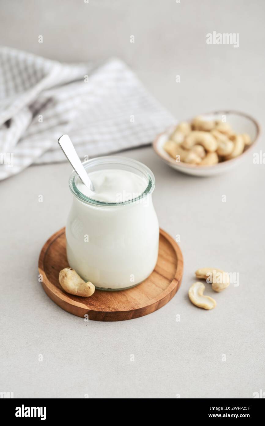 Panna acida anacardi in vaso di vetro con noci su sfondo chiaro, primo piano Foto Stock