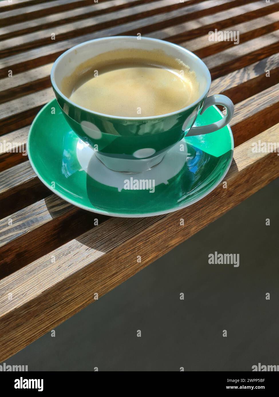 Una tazza verde con punti bianchi e caffè fresco si stende su una panca di legno, pausa caffè Foto Stock