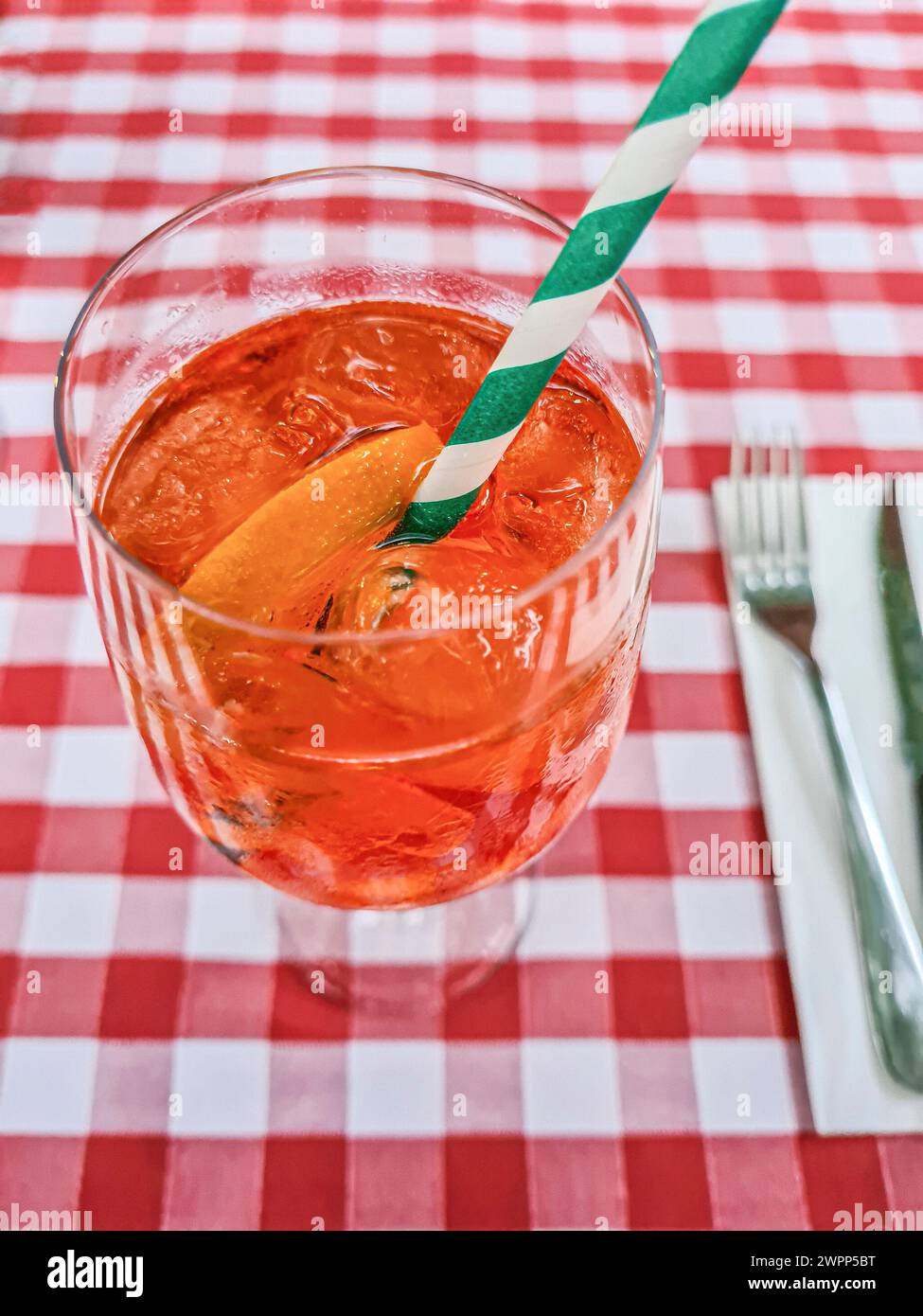 Una bevanda estiva alcolica di colore arancione con una fetta di arancio e paglia nel bicchiere si staglia su una tovaglia rossa e bianca Foto Stock