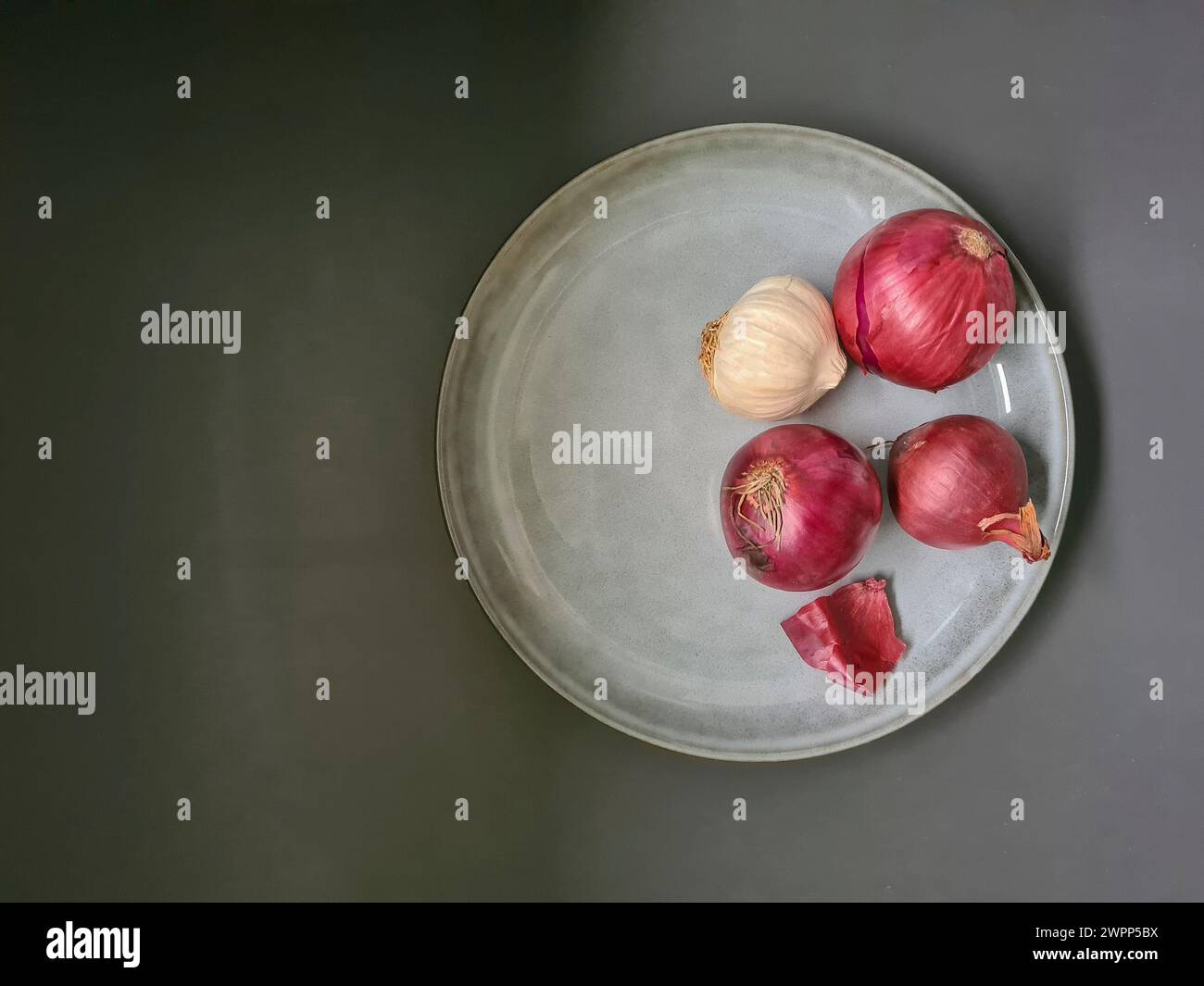 Natura morta con aglio e cipolle rosse su un piatto di ceramica Foto Stock