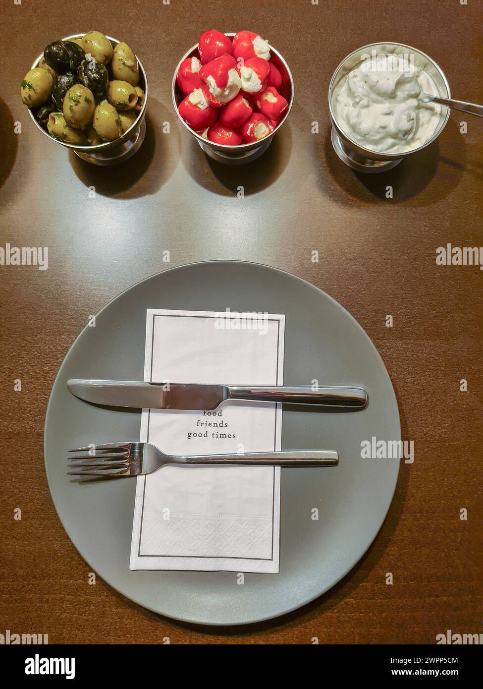 Una disposizione di piccole ciotole con antipasti e un piatto grigio con posate, tovagliolo stampato con un testo per gli ospiti Foto Stock