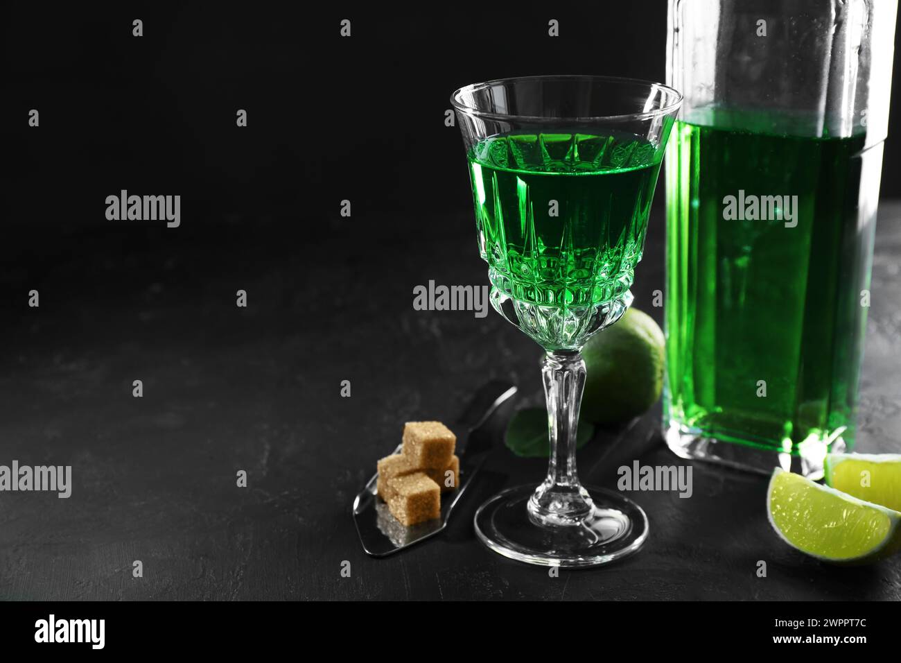 Absinthe, cucchiaio, zucchero di canna e lime sul tavolo nero, spazio per il testo. Bevanda alcolica Foto Stock