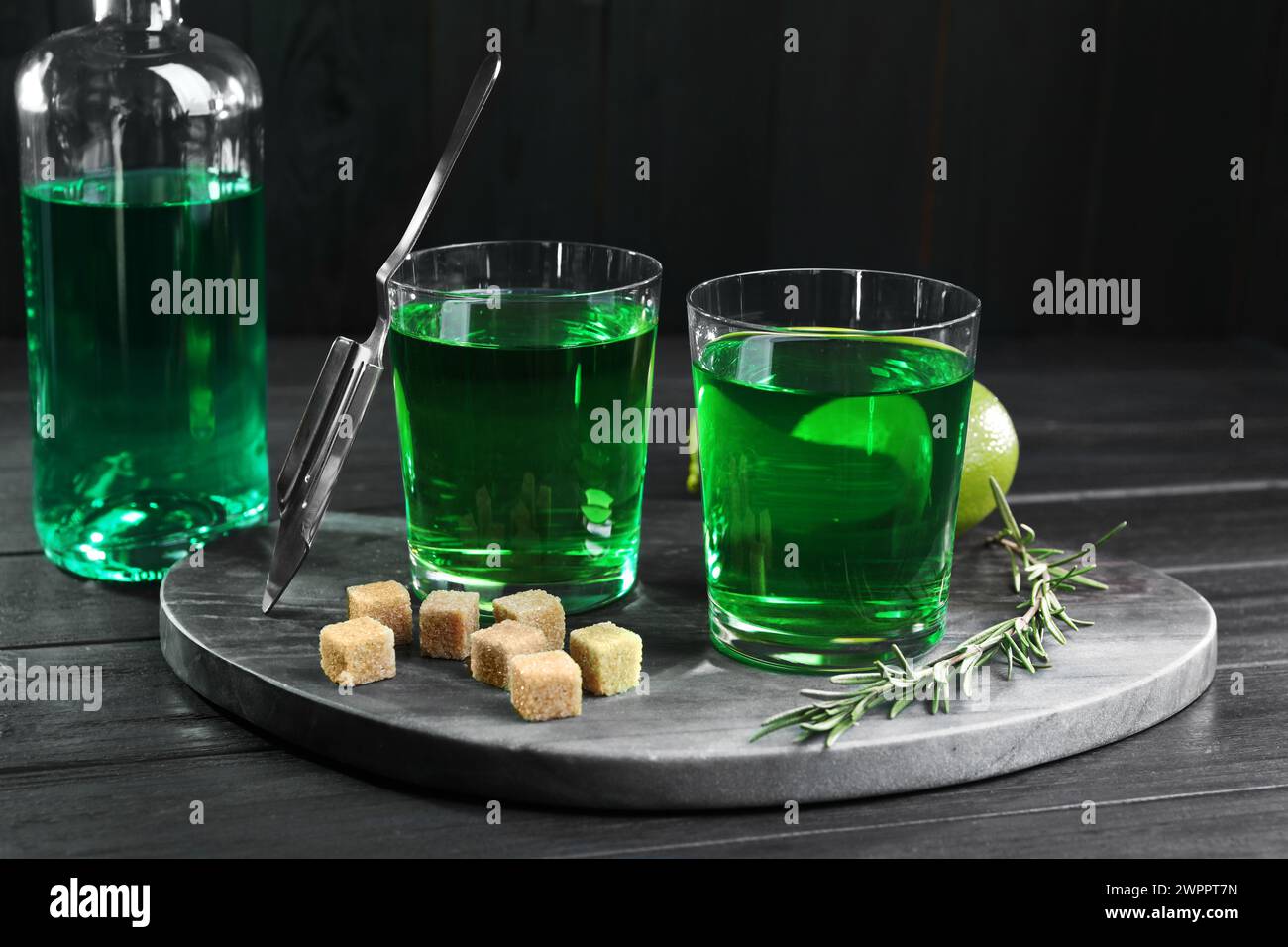 Absinthe in bicchieri, rosmarino, zucchero di canna e lime su un tavolo di legno nero. Bevanda alcolica Foto Stock