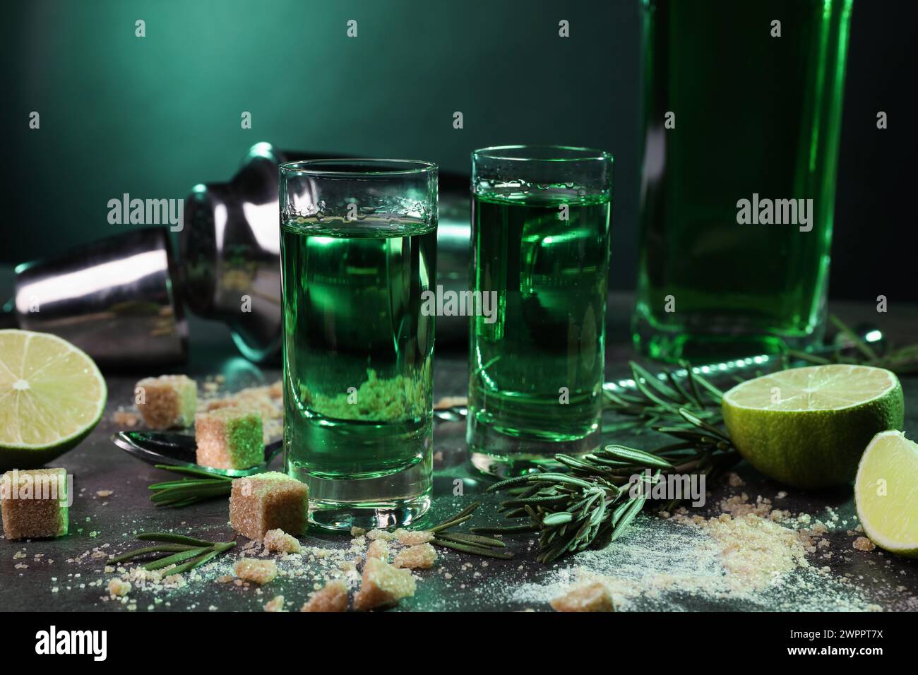 Absinthe in bicchieri da shot, cucchiaio, zucchero di canna, lime e rosmarino su un tavolo grigio, primo piano. Bevanda alcolica Foto Stock