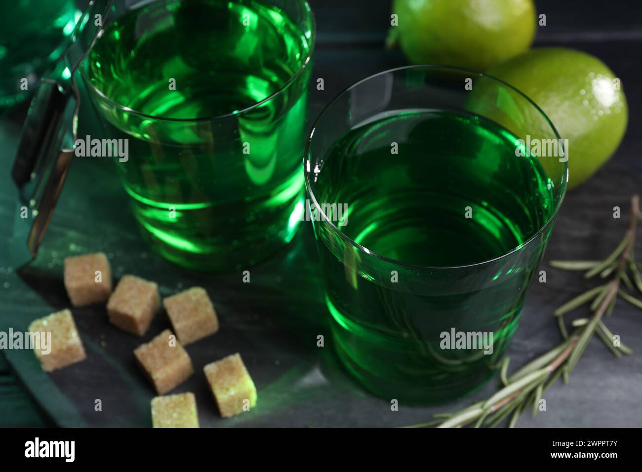 Absinthe in bicchieri, rosmarino, zucchero di canna e lime sul tavolo, primo piano. Bevanda alcolica Foto Stock